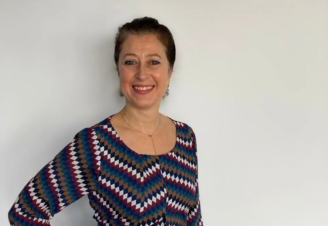 Femme souriante portant une robe colorée à motif géométrique devant un mur blanc.